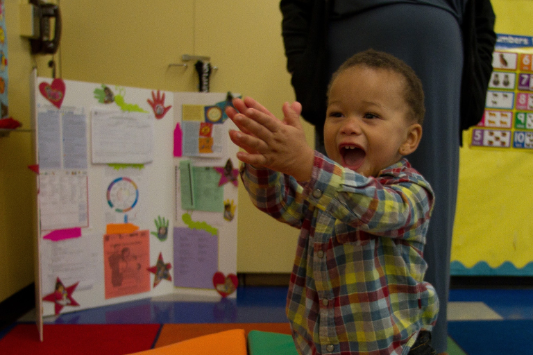 Toddler claps while learning something new in his infant and toddler education program